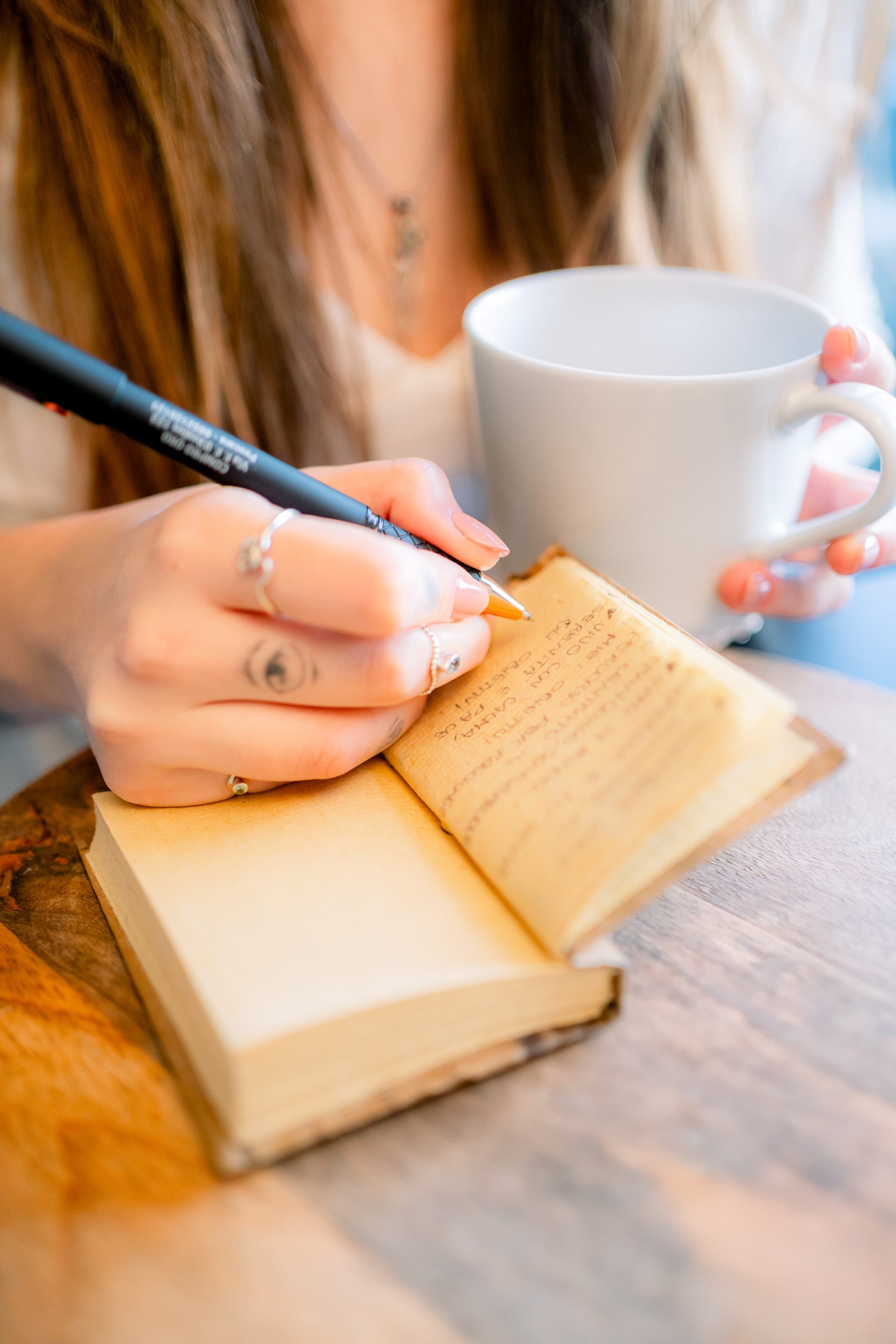Mano che scrive su un diario, accanto a una tazza